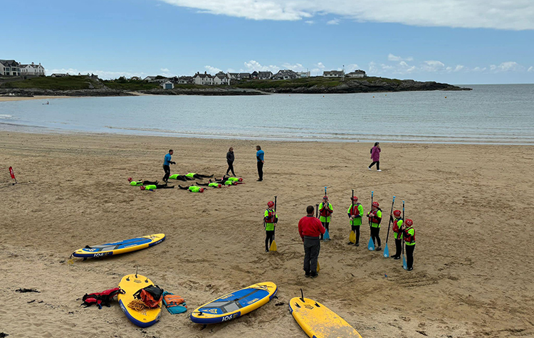 A group of people on Trearddur Bay beach with kayaks